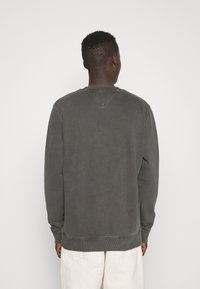 Šedá mikina s kulatým výstřihem, dlouhými rukávy, žebrovanými manžetami a lemem, a detail v-švu na zádech. Měkká, texturovaná tkanina.