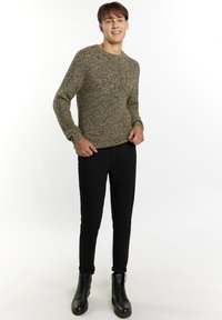 Maglione lavorato a maglia in tonalità beige e marrone, con scollo rotondo e maniche lunghe. Abbinato a pantaloni neri slim e stivaletti neri con lacci.