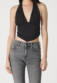Top negro sin mangas con un escote en V profundo y detalle de fruncido en la parte delantera, combinado con unos jeans de mezclilla gris ajustados que presentan un diseño clásico de cinco bolsillos.