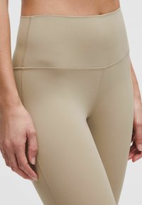 Leggings beige a vita alta con una texture liscia e elastica. Presentano cuciture piatte e una vita senza cuciture per comfort e supporto.