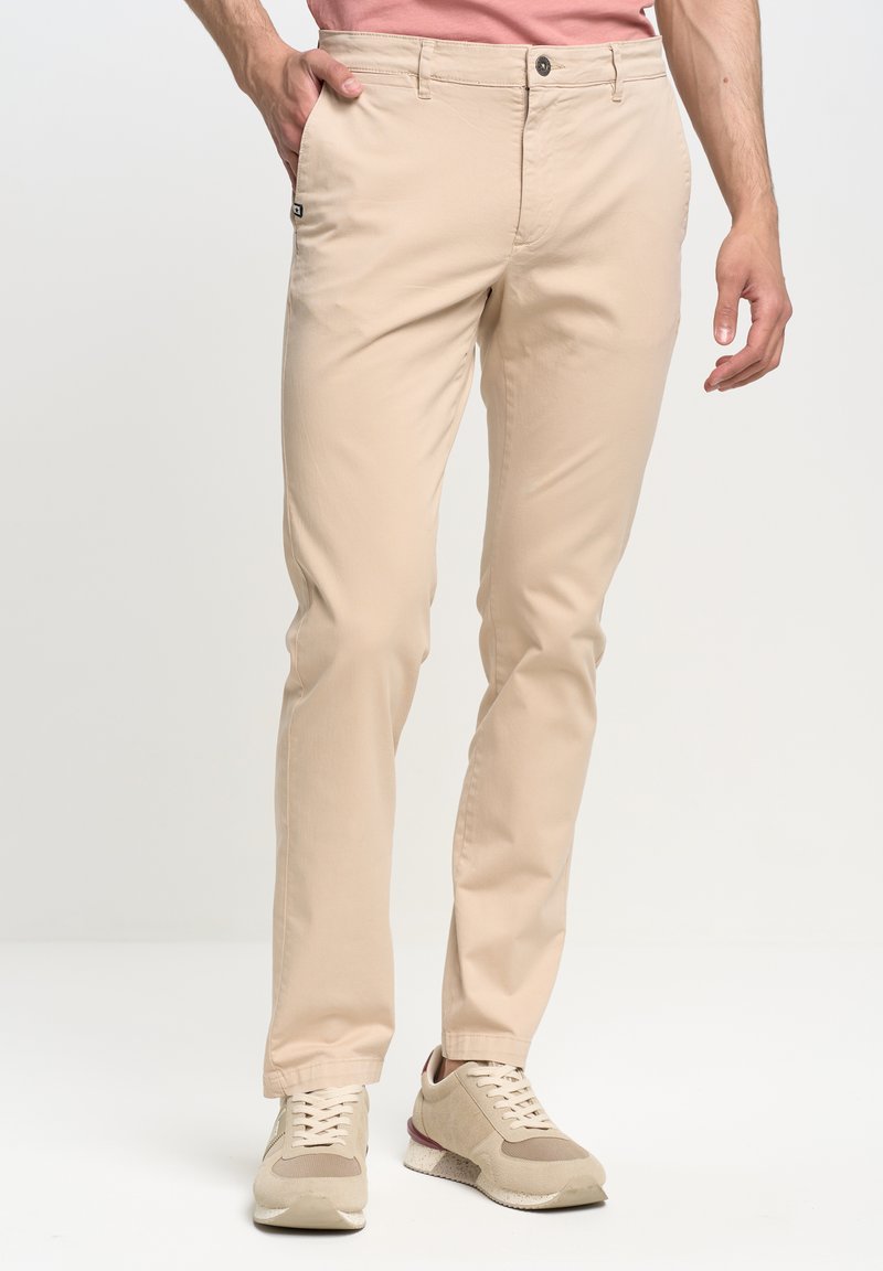 Beige chinos ar taisnu piegriezumu, izgatavoti no viegla auduma, ar pogu aizdari, sānu kabatām un diskētu logo uz kabatas.