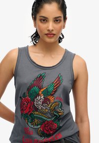 Grijze mouwloze tanktop met een kleurrijk geborduurd ontwerp van een vogel, slang en rozen. De tekst luidt "est 2023 Los Angeles."