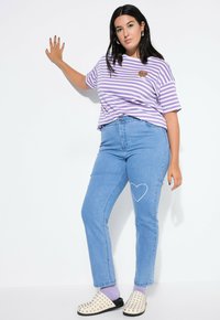 Lila och vit randig t-shirt med en leopardhjärtapatch, ljusblå jeans med en vit hjärtlinje på låret, och spikade slip-on skor.