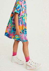 Värihikast, lühikeste varrukatega kleiti, millel on sinised, roosad ja kollased lillemustrid, on kombineeritud valgete kõrgete tenniste ja roosade pahkluu sokkidega.