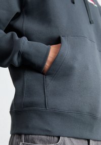 Mörkgrå sweatshirt med en känguruficka, ribbade ärmslut och nederkant, synliga sömmar och en mjuk textur.