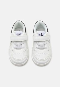 Baskets en cuir blanc avec un bout rond, un système de laçage et une sangle Velcro. Présente un détail perforé et un accent noir près du talon.