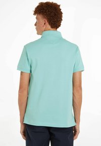 Piké skjorte i lys teal bomull, kortermet og med krage. Glatt tekstur med rett kant og liten ventilasjon bak.