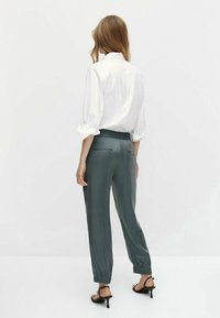 Weißes Hemd mit umgeschlagenen Ärmeln, kombiniert mit grauen, elastischen Hosen mit niedriger Taille. Glatter Stoff, schmal zulaufendes Bein und seitliche Taschen.