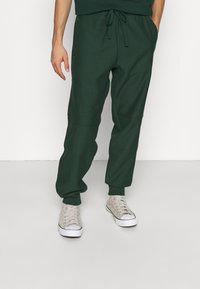 Mörkgröna joggerbyxor i mjukt material, med elastisk midja och dragsko, sidofickor och smalnande muddar.