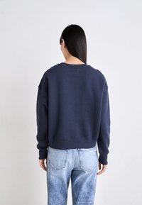 Sudadera corta de color azul marino con escote redondeado y puños acanalados, combinada con vaqueros desgastados de color azul claro. Diseño minimalista, textura suave.