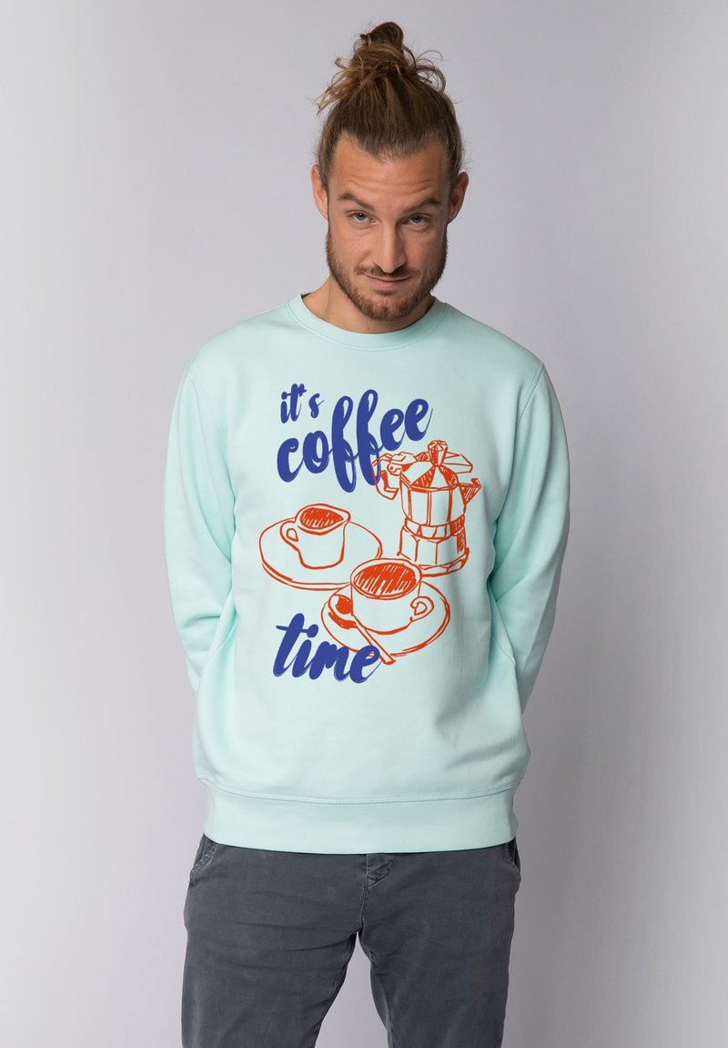 Sweat-shirt vert menthe avec des graphismes sur le thème du café en orange et marine, portant le texte "c'est l'heure du café" et des illustrations de tasses et d'une machine à café.
