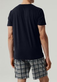 Granatowa koszulka z krótkim rękawem w połączeniu z szarymi spodniami w kratę z niebieskimi i czarnymi liniami. Miękka tkanina bawełniana, luźny krój.
