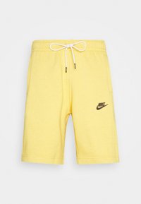 Shorts en coton jaune avec une taille élastique dotée d'un cordon de serrage, des poches latérales et un logo Nike noir sur la jambe gauche.