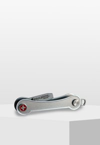 Silver multi-tool key holder with a curved design, featuring a red Swiss cross logo, matte texture, and a metal texture on the body.