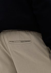 Halványbarna nadrág sima textúrával, elegáns zsebfelülettel és elasztikus derékrésszel, sötét, texturált felsővel párosítva.