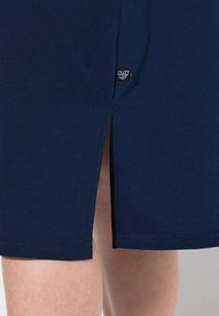 Gonna di cotone blu navy con uno spacco laterale e un piccolo etichetta nera vicino all'orlo. Il tessuto ha una texture liscia e una finitura morbida.