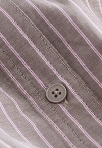 Gros plan d'un seul bouton marron cousu sur un tissu marron avec des rayures verticales rose clair et des détails de couture visibles.