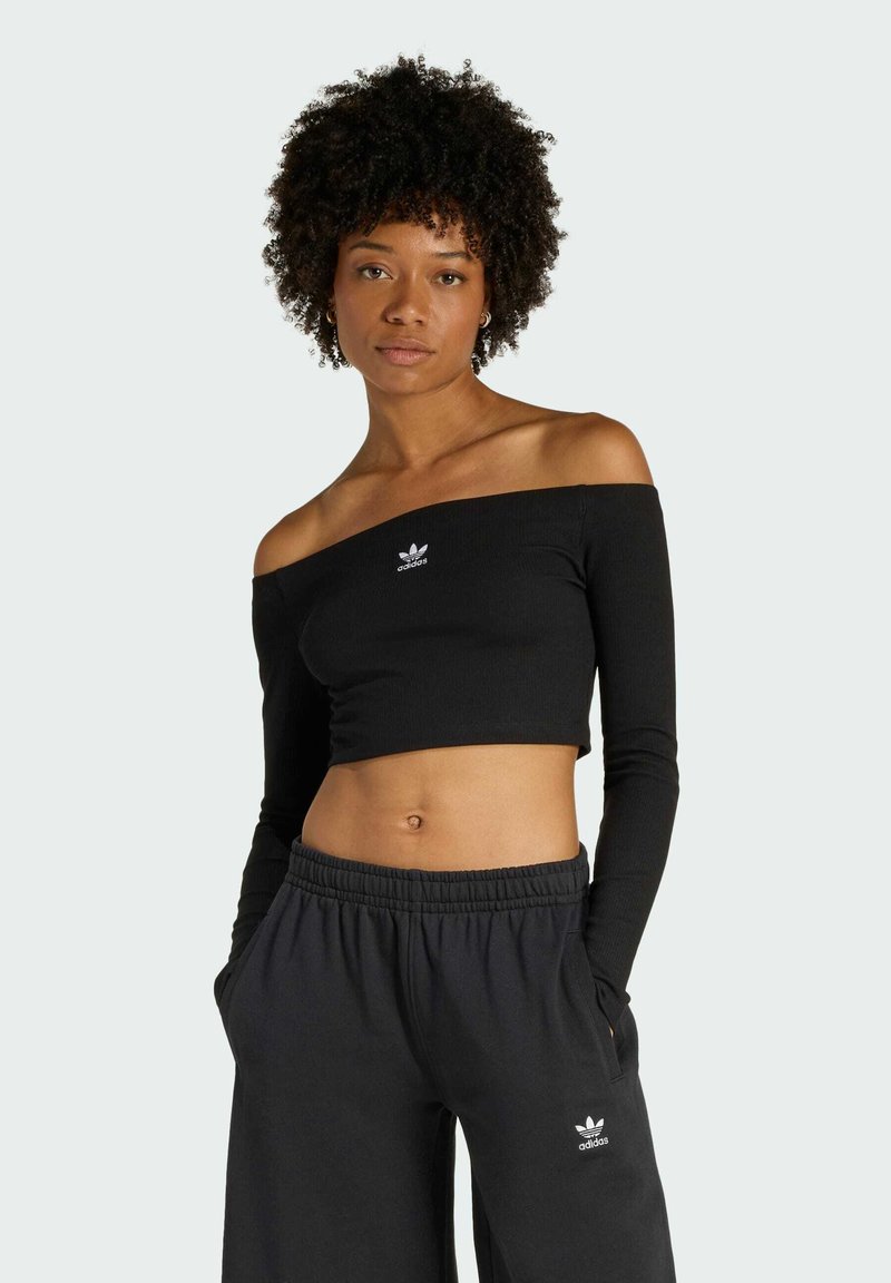 Czarny top typu crop off-the-shoulder z długimi rękawami, z małym białym logo Adidas na piersi. Noszony z czarnymi dresami.