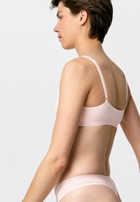 Hellrosa kabelloser BH mit verstellbaren Trägern und glatter Textur, kombiniert mit passendem minimalistischen Bikini-String, der ein nahtloses Design aufweist.