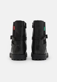 Botas de tobillo de cuero negro con un acabado texturizado, que cuentan con una correa y hebilla, acentos en verde y rojo, y una suela de goma resistente.