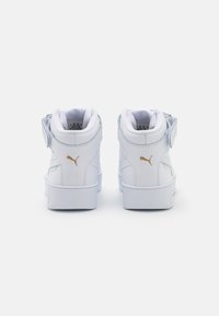 High-top white sneakers with a smooth leather texture, featuring a gold logo and Velcro strap. Soft lining and detailed stitching accents.