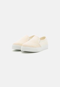 Slip-on sko laget av beige mesh og kremfarget stoff, med såle av hvit gummi og ingen synlige detaljer eller dekorasjoner.
