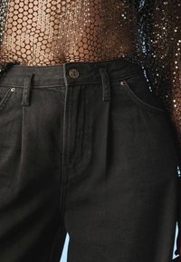 Mustat korkeavyötäröiset farkut, joissa on tekstuuripinta, etutaskut, metallinen nappisulku ja kontrastiväriset ompelutiedot.