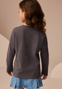 Långärmad grå bomullsskjorta med rund halsringning, i kombination med en ljusblå denimkjol med plisserad design.