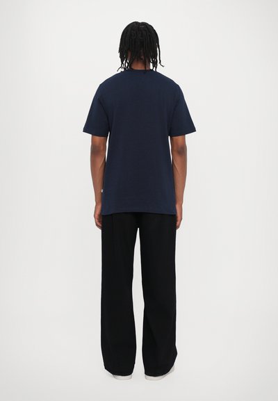 Mørkeblå bomulds T-shirt med korte ærmer og rund halsudskæring, kombineret med løse sorte bukser og hvide sneakers.