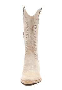 Botas de vaquero de ante beige con intrincados patrones cortados, acentos de costura elevada, punta afilada y costuras decorativas en el caño.