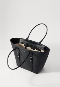 Musta olkalaukku, jossa on teksturoitu kuvio, tuplat käs handles, ja vetoketjullinen sisätasku. Täydentää nahka yksityiskohtia ja vaalea vuori.