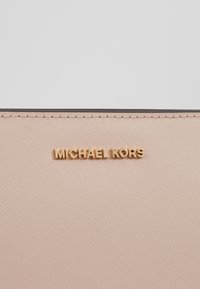 Portafoglio rosa testurizzato con logo dorato "MICHAEL KORS", contornato da un bordo scuro a contrasto. Design semplice con cuciture ordinate.