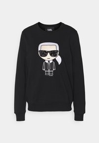 Felpa nera a maniche lunghe con figura dei cartoni animati che indossa occhiali da sole, capelli bianchi raccolti, abito e cravatta neri sul davanti.