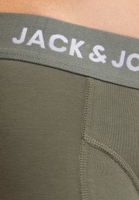 Olivgrüne Unterwäsche mit geriffelter Textur, ausgestattet mit einem grauen Gummibund, auf dem "JACK & JONES" in Weiß aufgedruckt ist. Detaillierte Nähte sind sichtbar.
