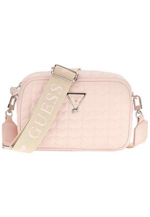 Bolso bandolera acolchado de color rosa claro con una correa ancha beige que lleva el texto "GUESS" y un logo triangular metálico en la parte frontal.