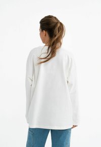 Witte oversized lange mouwen shirt met een ronde halslijn, zachte textuur, verlaagde schouders, gecombineerd met lichtblauwe denim jeans.
