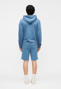 Niebieska bawełniana bluza z kapturem, kieszenią kangurką i sznurkiem do regulacji kaptura, w zestawie z dopasowanymi szortami. Strój cechuje się luźnym krojem i miękką fakturą.