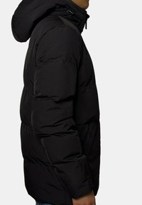 Doudoune noire matelassée avec capuche, au texture lisse et design matelassé, disponible en coupe décontractée avec poches latérales.