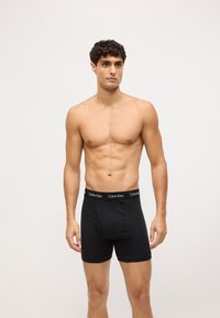 Bóxer de algodón negro con un diseño ajustado, con una cinturilla negra en contraste etiquetada como "Calvin Klein." Textura suave, sin patrones visibles.