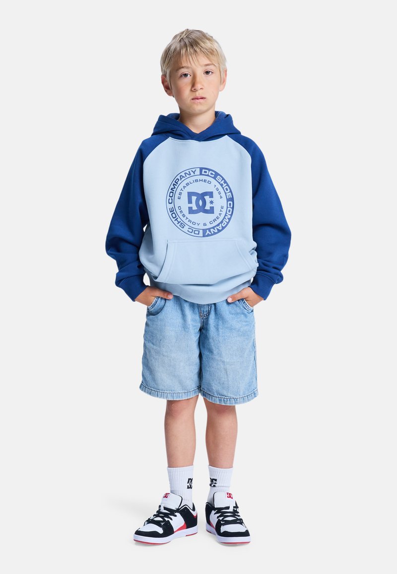 Niebieska i jasnoniebieska bluza z kapturem z przednią kieszenią i logo, w połączeniu z dżinsowymi szortami oraz czarno-białymi sneakersami.