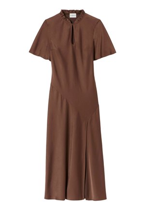 Mujer de pie con un vestido midi marrón de manga corta, abertura lateral, cinturón negro, gorra blanca y zapatillas azules sobre un fondo gris liso.