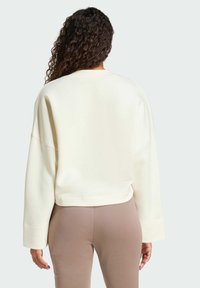 Krämfärgad sweatshirt med en kortad design och vida ärmar, som har en slät textur och inga synliga mönster.