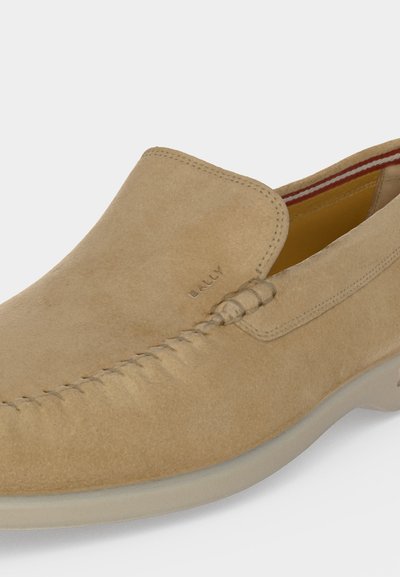 Ανοιχτό καφέ σουέτ loafer slip-on με ραφές σε στυλ μοκασίνου και διακριτική σήμανση στο πάνω μέρος, με λαστιχένια σόλα και ριγωτή εσωτερική επένδυση.