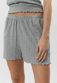 Sive kratke hlače od rebraste tkanine, s elastičnim pojasom, bočnim džepovima i obrubom s valovitim rubom. Tekstura s vertikalnim prugama.