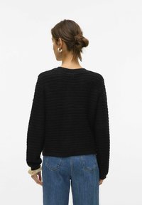 Maglione nero con un motivo a coste testurizzato, scollatura rotonda e vestibilità morbida, abbinato a jeans blu a vita alta.