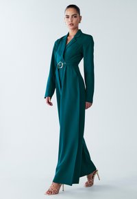 Teal long-sleeve dress with a fitted silhouette, lapel collar, and a wide belt featuring a gold buckle. Smooth fabric, leg slit, and elegant design.