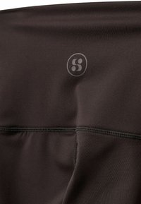 Czarna tkanina sportowa o gładkiej teksturze, z wyraźnym logo i płaskimi szwami. Materiał wydaje się elastyczny i trwały.