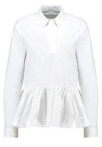 Blusa bianca a maniche lunghe con colletto, caratterizzata da un orlo peplum arricciato e una texture del tessuto liscia. Design slim fit.