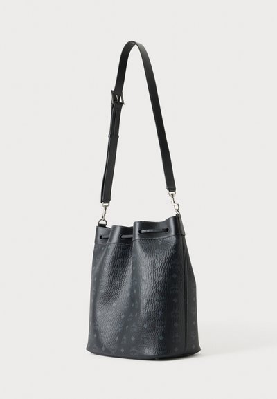 Sac seau texturé noir avec bandoulière réglable et motif discret sur la surface, debout sur un fond clair.