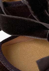 Czarne welurowe buty o miękkiej teksturze, z okrągłym wzorem, satynową kokardą z przodu i jasnobrązowym wnętrzem.